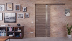 Front-Milieuansicht der vor der Wand laufenden HÖRMANN Schiebetür Pure 1 Gebürstete Lärche dunkel quer Duradecor DesignLine mit Lichtausschnitt Bandseite